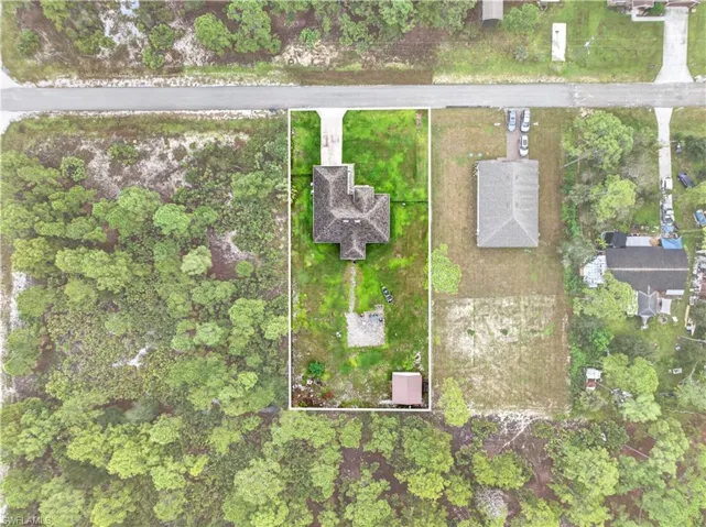 Aerial perspective featuring a multi-pitched roof residence, concrete driveway, detached storage structure, and expansive grounds characterized by natural vegetation