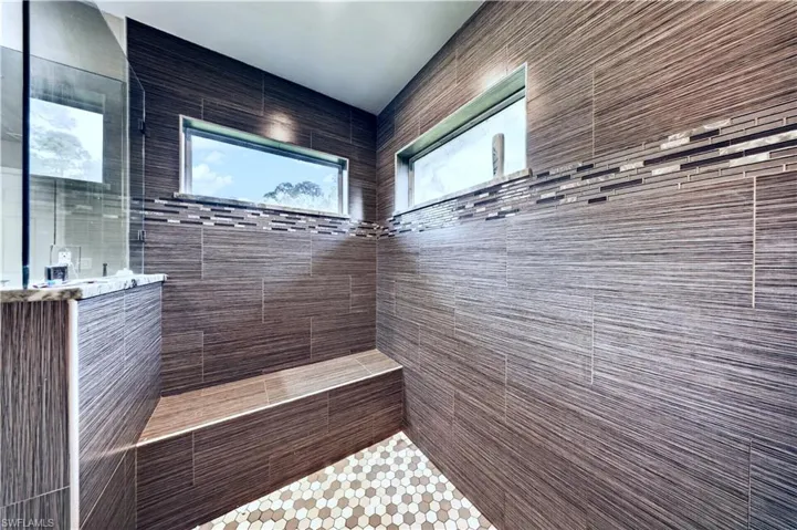Walk-in shower featuring textured horizontal tile wall cladding, built-in tiled bench, hexagon-patterned floor tile, horizontal transom windows, and a glass partition