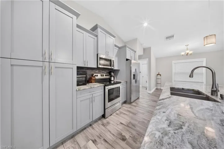 Kitchen featuring shaker-style cabinetry, stainless steel appliances, expansive stone-surface island, undermount sink, and wood-finish flooring
