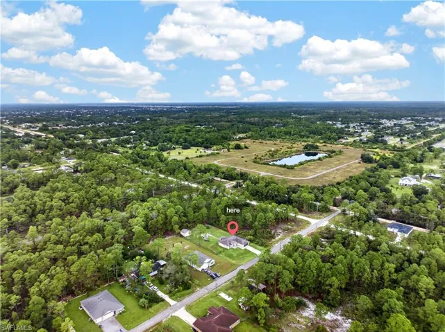 Aerial perspective of a property situated on a lot with mature tree coverage, paved road access, and proximity to expansive open land