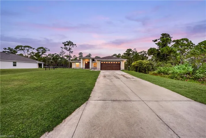Single-story residence featuring a paved driveway, multi-car garage with transom windows, and an expansive lawn