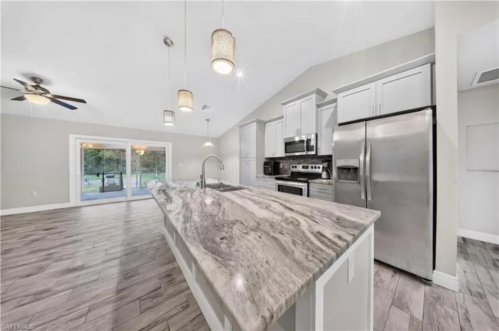 Kitchen featuring a large island with stone countertops, white shaker-style cabinetry, stainless steel appliances, wood-finish tile flooring, and vaulted ceilings with pendant lighting