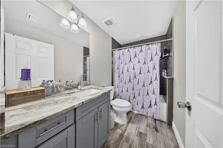 Bathroom featuring a vanity with stone-patterned countertop, charcoal cabinetry, integrated sink, and wood-finish flooring
