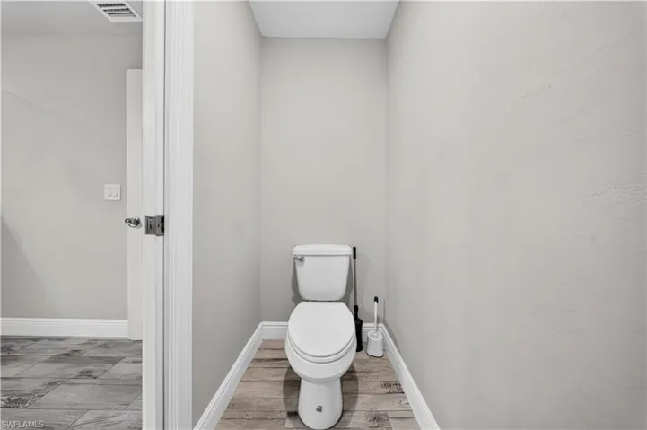 Neutral-toned interior space featuring wood-finish flooring and a white porcelain toilet