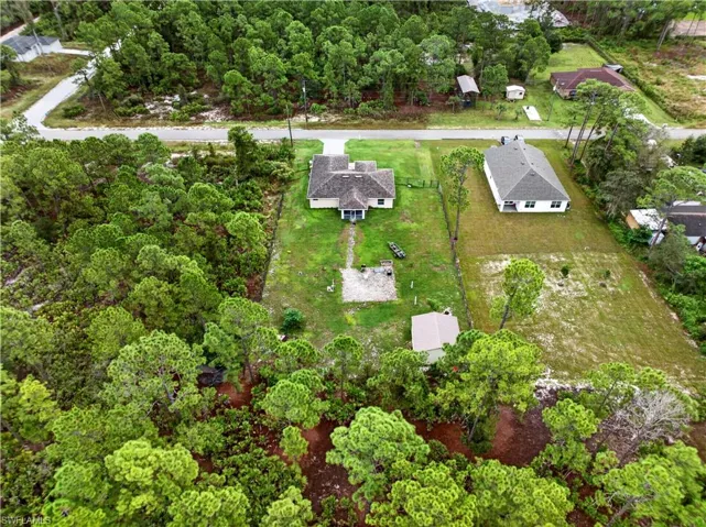 Aerial perspective of a property featuring a single-story residence, a detached storage structure, open lawn areas, and wooded perimeter boundaries