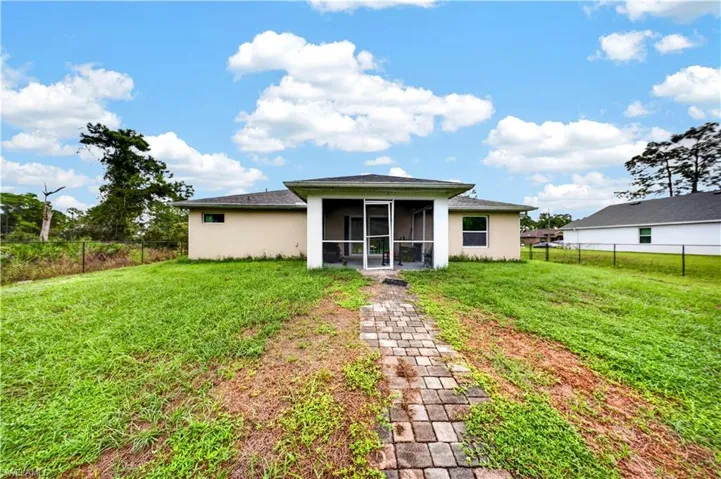 Stucco exterior featuring a covered screened-in patio, a paver stone walkway, and a fenced rear yard