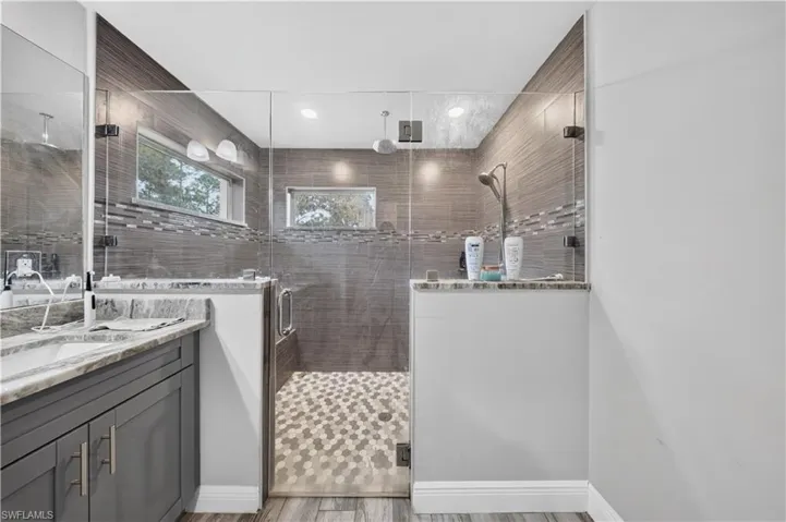 Walk-in shower featuring a frameless glass enclosure, horizontal tiled wall surround, and geometric floor tiling, paired with a dark-finish vanity and stone-topped surfaces