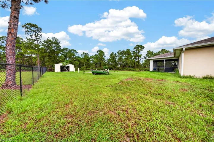 Expansive backyard featuring a chain-link fence, detached storage structure, and a screened-in rear porch