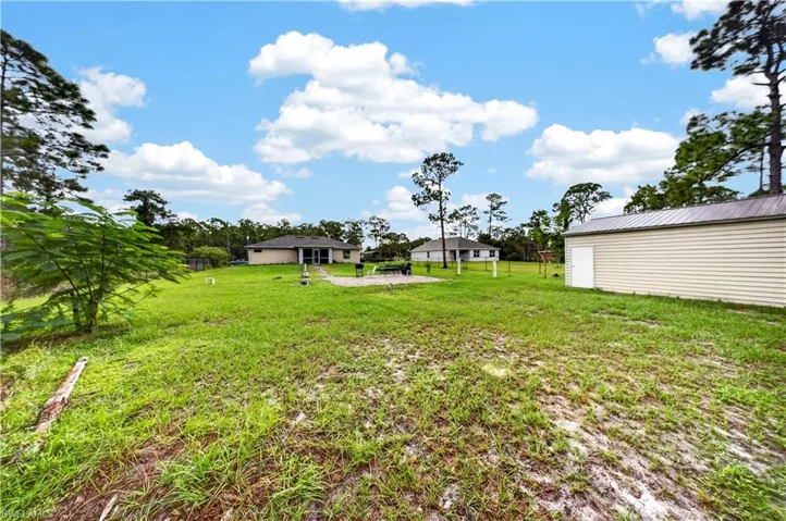 Expansive backyard featuring a stone-paver patio, a detached storage building with a metal roof, and mature pine trees