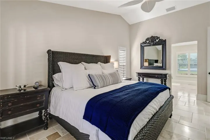 Bedroom with stone tile flooring, vaulted ceiling, and a ceiling fan
