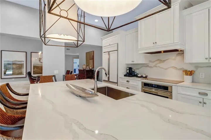 Kitchen with light stone countertops, white cabinets, oven, hanging light fixtures, and recessed lighting