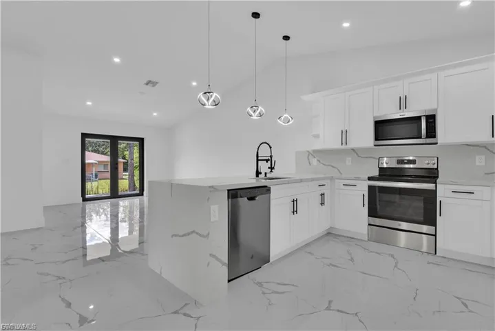Kitchen featuring stainless steel appliances, a peninsula, white cabinets, light stone countertops, and lofted ceiling