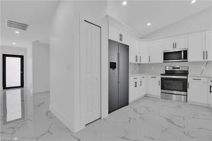 Kitchen featuring stainless steel appliances, recessed lighting, white cabinetry, light marble finish floors, and vaulted ceiling