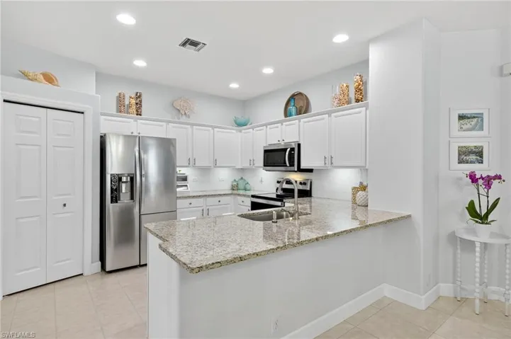 Kitchen with stainless steel appliances, white cabinetry, light tile patterned floors, light stone counters, and recessed lighting