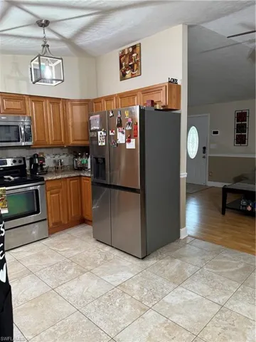 Kitchen featuring stainless steel refrigerator with ice dispenser, range, brown cabinetry, tasteful backsplash, and white microwave
