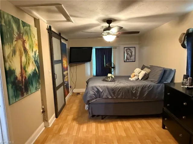 Bedroom with a ceiling fan, light wood finished floors, and a barn door