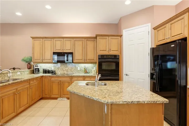 Kitchen featuring black appliances, light stone countertops, backsplash, recessed lighting, and a kitchen island with sink