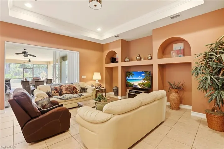 Living area with built in features, a tray ceiling, light tile patterned flooring, ceiling fan, and recessed lighting