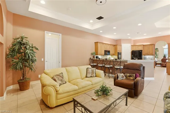 Living room with arched walkways, a tray ceiling, light tile patterned flooring, ornamental molding, and recessed lighting
