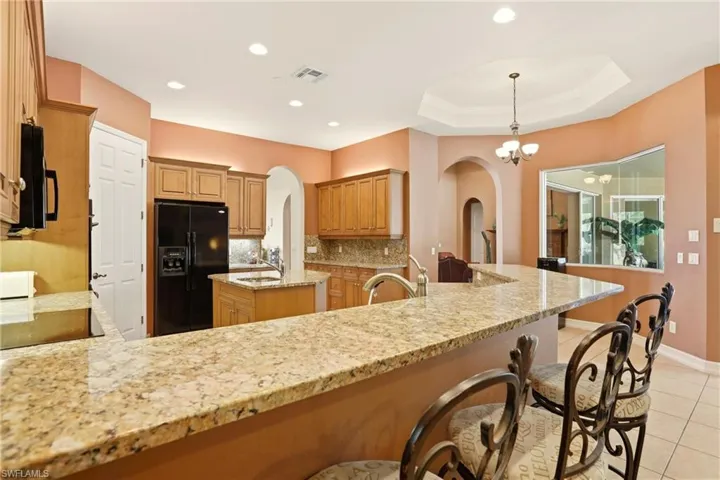 Kitchen featuring black appliances, light tile patterned floors, arched walkways, backsplash, and a tray ceiling