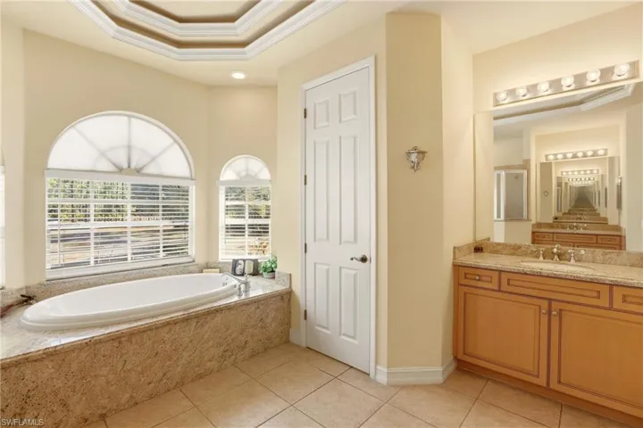 Bathroom with ornamental molding, vanity, a bath, light tile patterned floors, and a tray ceiling