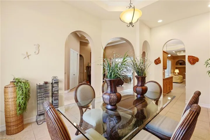 Dining area with arched walkways, light tile patterned flooring, recessed lighting, and a tray ceiling