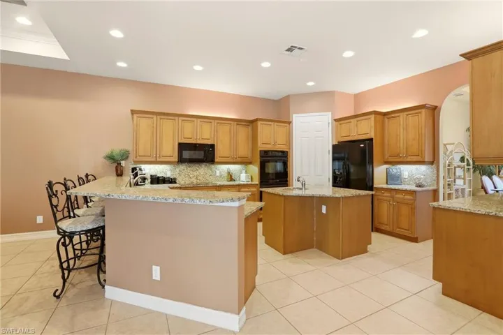 Kitchen featuring a breakfast bar area, a center island with sink, decorative backsplash, black appliances, and arched walkways