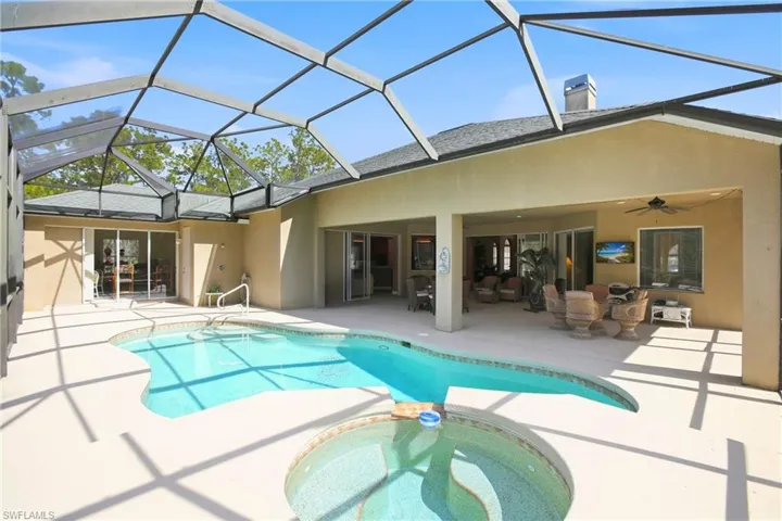 Back of property featuring stucco siding, a chimney, a patio area, a pool with connected hot tub, and a sunroom