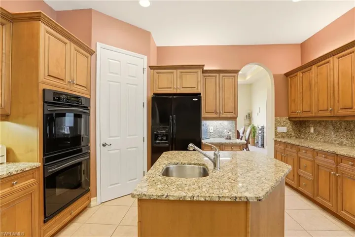 Kitchen with black appliances, light stone countertops, arched walkways, wood finish cabinetry, and tasteful backsplash