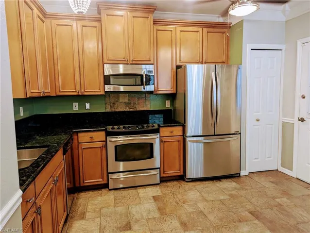 Eat in Kitchen with ornamental molding, dark stone countertops, appliances with stainless steel finishes, backsplash, and light tile floors