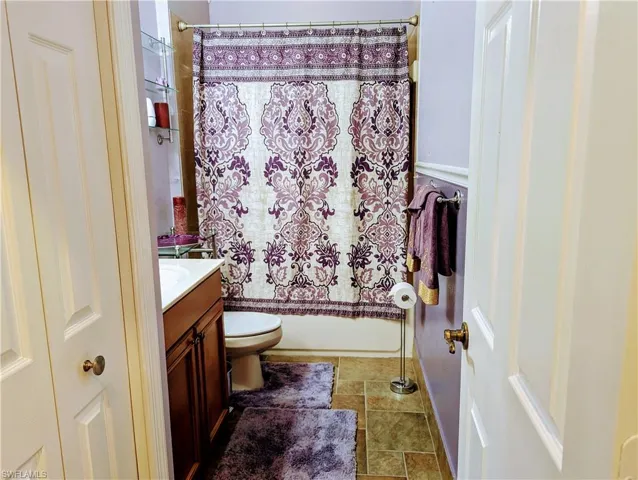 Full bathroom featuring shower / bath combo with shower curtain, vanity, toilet, and tile floors