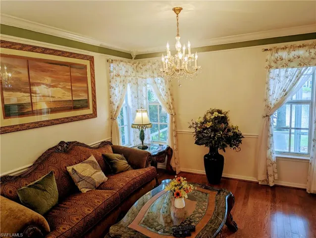Living room with wood-type flooring, ornamental molding, and an inviting chandelier