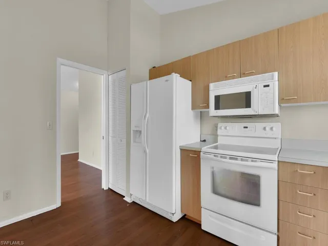 Kitchen with dark wood-type flooring, light brown cabinets, white appliances, and a towering ceiling