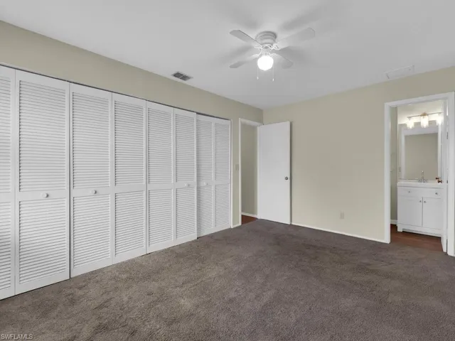 Unfurnished bedroom with connected bathroom, a closet, ceiling fan, and dark colored carpet