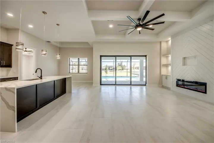 Unfurnished living room featuring coffered ceiling, a fireplace, a sink, and a ceiling fan