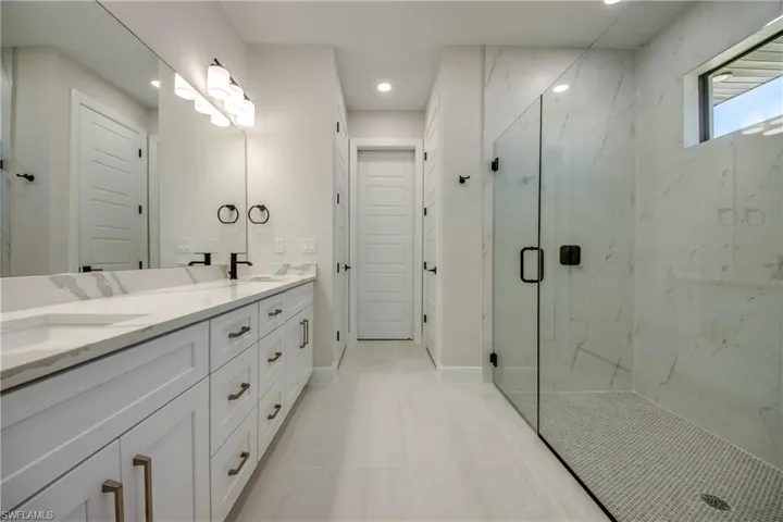 Full bathroom featuring baseboards, double vanity, a marble finish shower, recessed lighting, and a sink