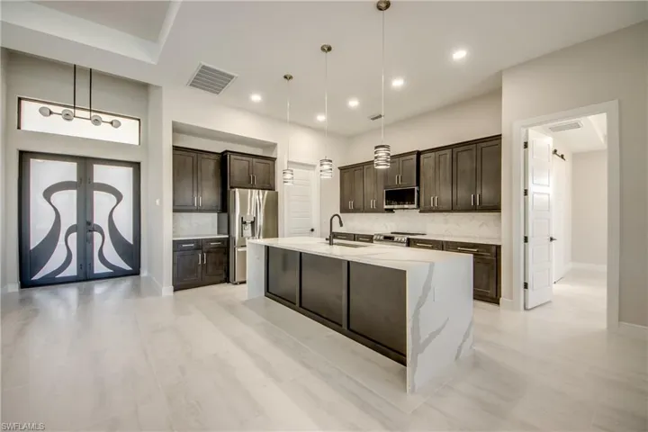 Kitchen featuring a center island with sink, a sink, visible vents, dark brown cabinets, and appliances with stainless steel finishes