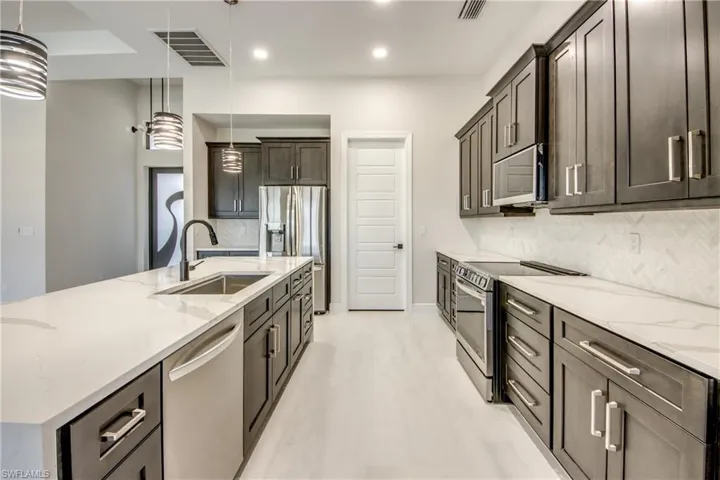 Kitchen with light stone counters, a sink, hanging light fixtures, stainless steel appliances, and visible vents