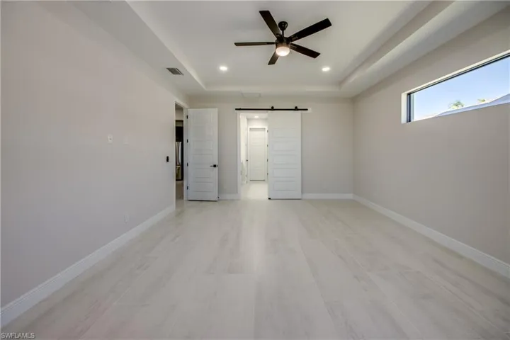 Unfurnished bedroom featuring recessed lighting, baseboards, a raised ceiling, a barn door, and visible vents