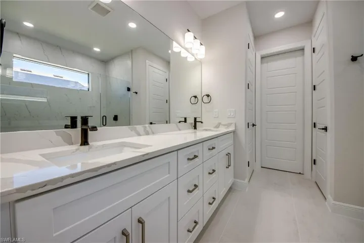 Full bathroom featuring double vanity, visible vents, a sink, and a marble finish shower