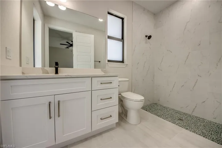Full bathroom featuring toilet, tile patterned flooring, vanity, and a marble finish shower