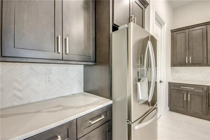 Kitchen with dark brown cabinetry, light stone countertops, stainless steel fridge, and tasteful backsplash