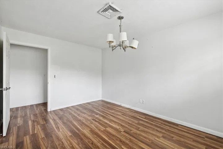 Empty room with dark wood-type flooring and an inviting chandelier