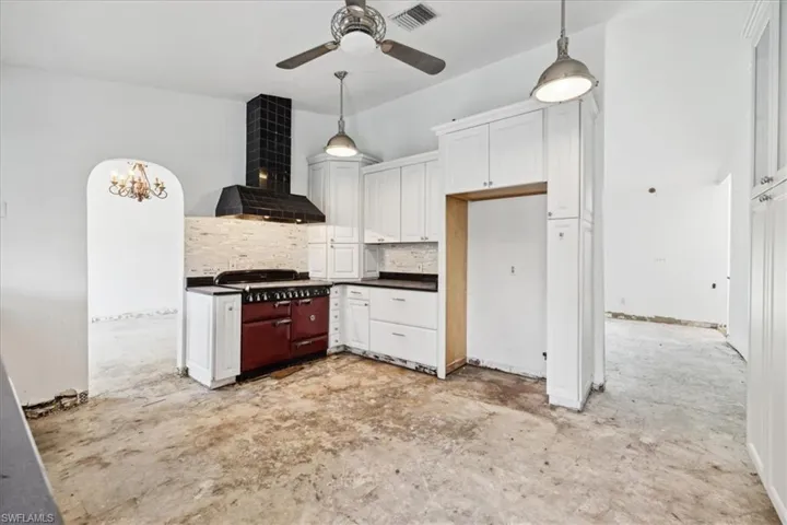 Kitchen with backsplash, hanging light fixtures, white cabinetry, wall chimney range hood, and ceiling fan