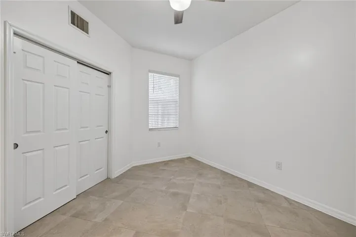 Interior room featuring neutral tile flooring, a six-panel sliding closet door, and a ceiling fan with integrated lighting