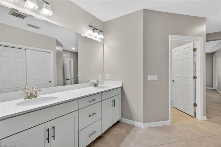 Double vanity featuring white shaker-style cabinetry, solid-surface countertops, integrated dual sinks, and polished nickel hardware