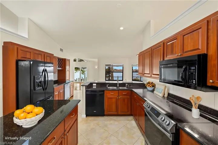 Kitchen with black appliances, light tile patterned floors, brown cabinetry, a peninsula, and vaulted ceiling