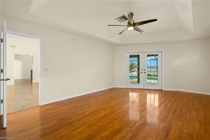 Unfurnished room featuring a tray ceiling, french doors, light wood-type flooring, and ceiling fan
