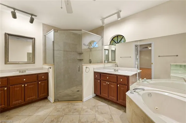 Bathroom featuring a stall shower, a ceiling fan, two vanities, and rail lighting
