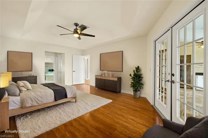 Bedroom with a raised ceiling, wood finished floors, french doors, ensuite bath, and a ceiling fan